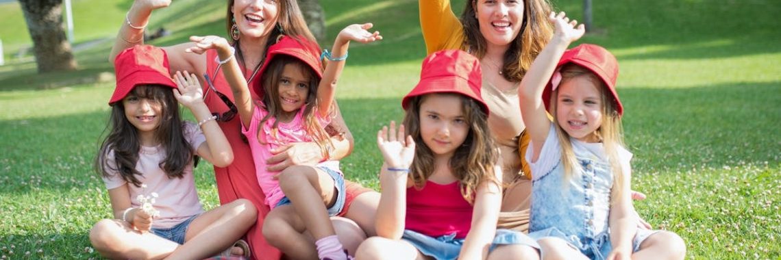 Two women and four girls enjoy a sunny picnic in Portugal, waving happily in the park.